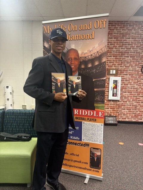 Coach Riddle holding copies of his book at a promotional event